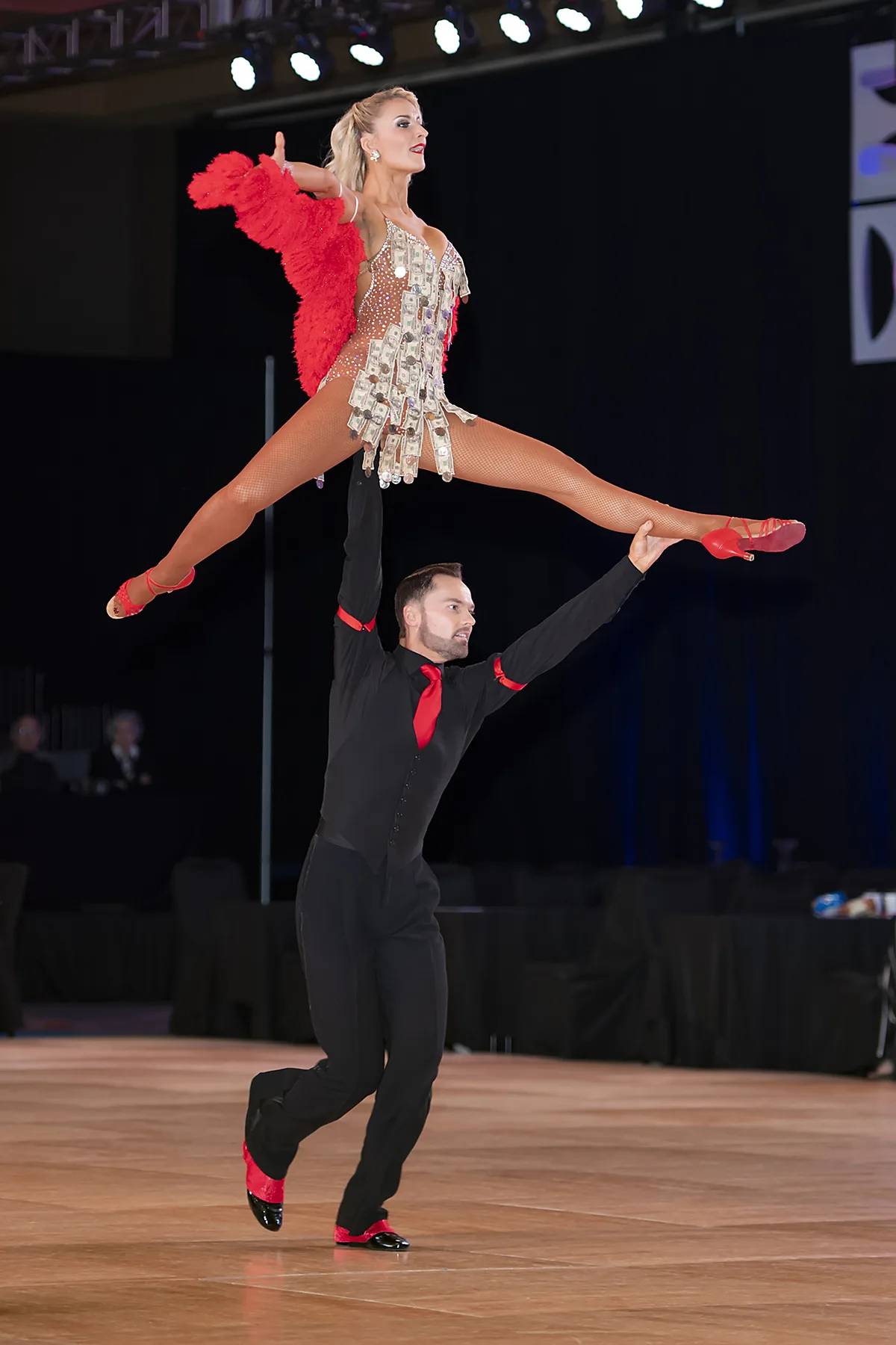 Jaimee flies in a full split leap in red directly over Travis's head
