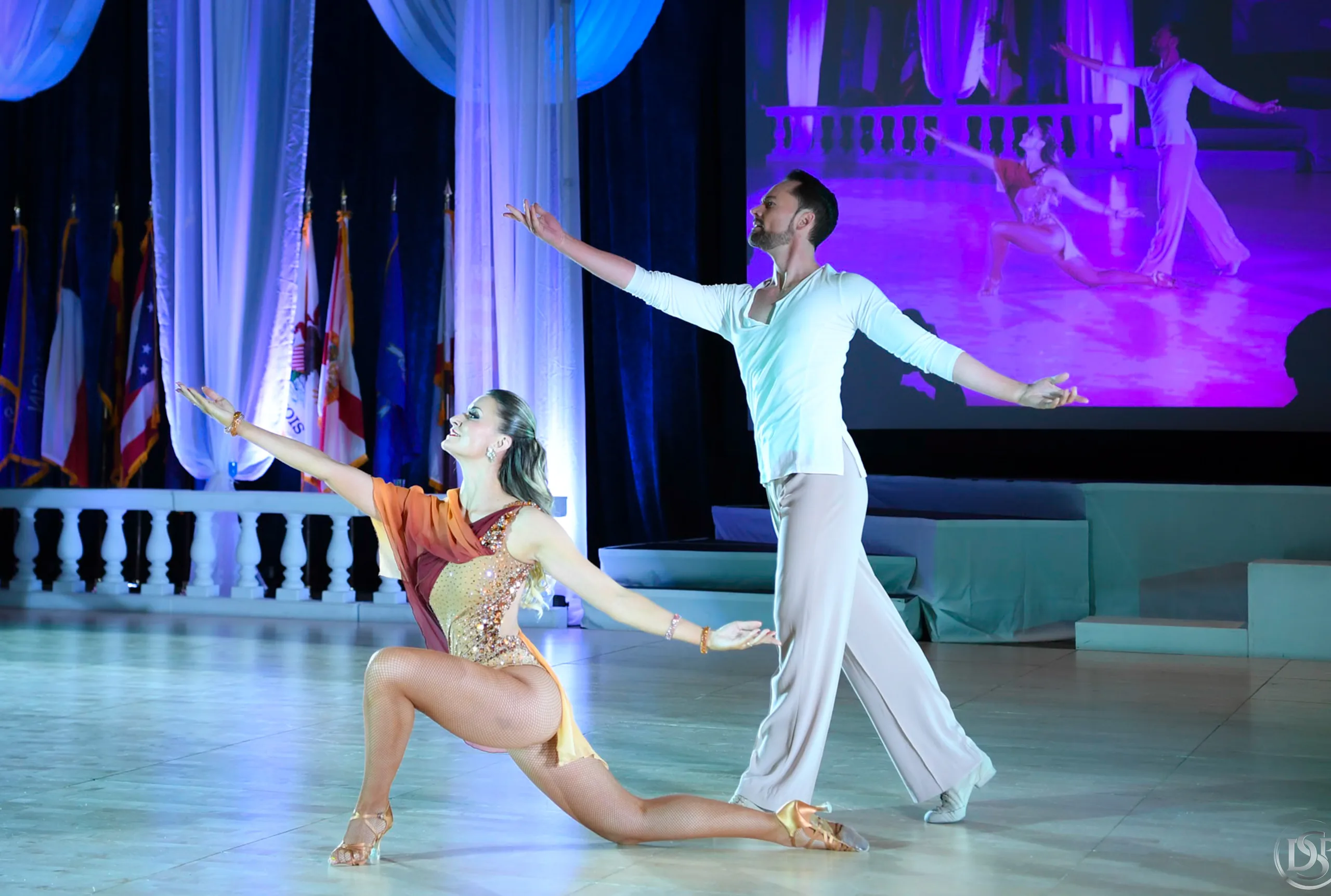 Travis reaches into a long lunge as Jaimee kneels low beneath him on a stage framed by columns