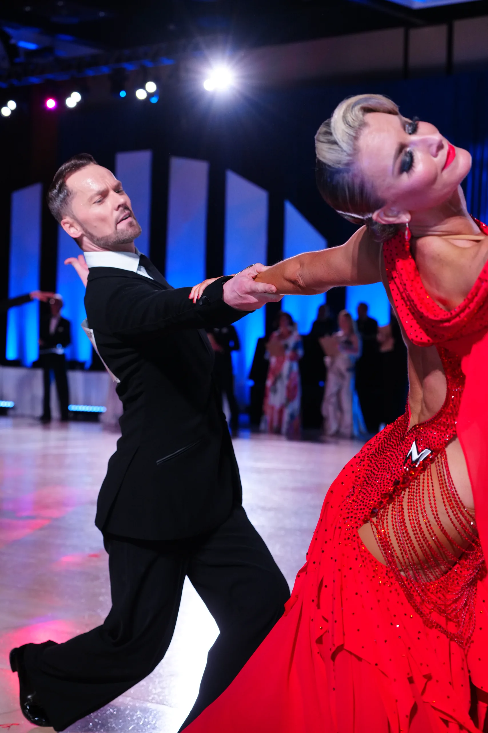 Travis leans over Jaimee's deep dip, her red dress pooling against a dark floor